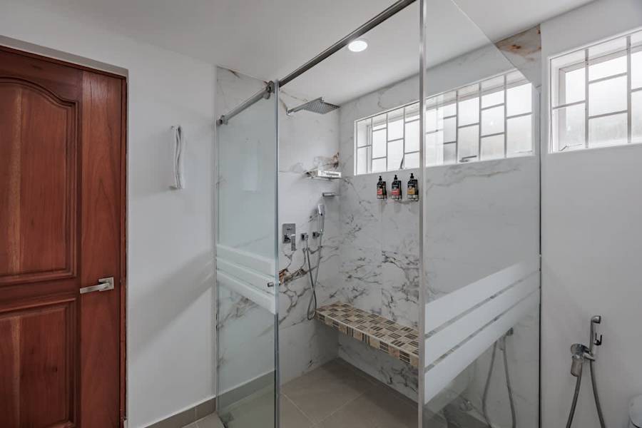 Private Ensuite # 2 – Bright en-suite bathroom with glass-enclosed rain shower, modern finishes, L’Occitane amenities, and hair dryer.