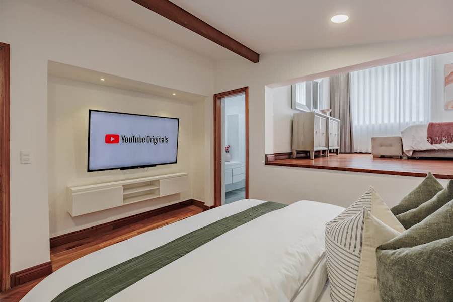 Family Suite #4: Integrated Comfort. This perspective showcases the large Smart TV and direct access to the private ensuite. The elevated loft area creates a dynamic sense of space, offering a versatile retreat for both relaxation and entertainment.