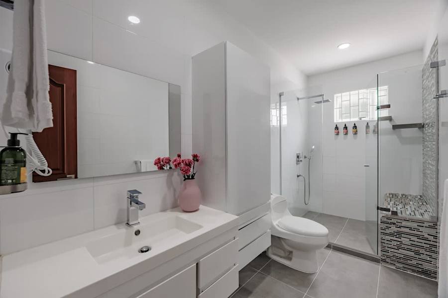Family Ensuite 4 – Bright en-suite bathroom with large vanity, glass-enclosed rain shower, built-in shower bench, L’Occitane amenities, and hair dryer.